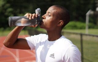 man standing on a running track drinking a refillable water bottle
