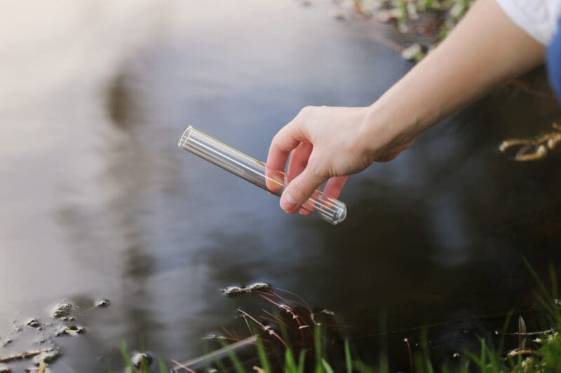 a specialist s hand draws water into a flask from a river for further research in the laboratory. checks the level of water pollution. selective focus