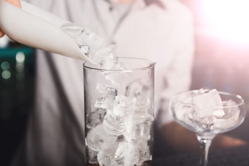 Barman’s hands pouring ice for cocktail Barman's hands in bar interior making alcohol cocktail.
